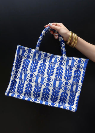 Large blue and white tote bag made in Greece by artisans using looms. Greek motif design with evil eyes, olive branches, and modern shapes. Handmade fashion shopper bag