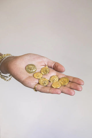 Hand holding a collection of gold coin necklace pendants made in Greece with Greek historical figures