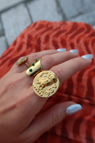 Hand wearing gold jewelry including a gold athenian tetradrachm coin ring with Ancient Greek goddess Athena's owl, a symbol of wisdom. Owl ring made in Greece, Greek jewelry