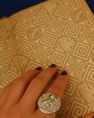 Hand wearing a silver Athena athens tetradrachm coin ring with Athena's owl with a patterned background