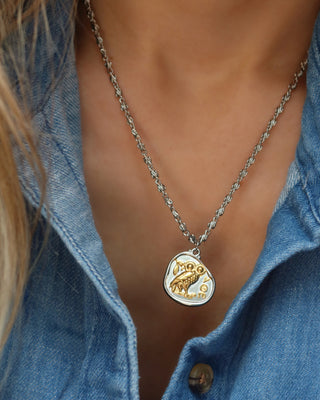 Woman wearing a silver coin pendant necklace with Athena's Owl of Wisdom, a replica of an ancient Greek Athenian tetradrachm coin that is silver with a gold owl, two-tone mixed metal necklace made in Greece on an infinity s-link chain
