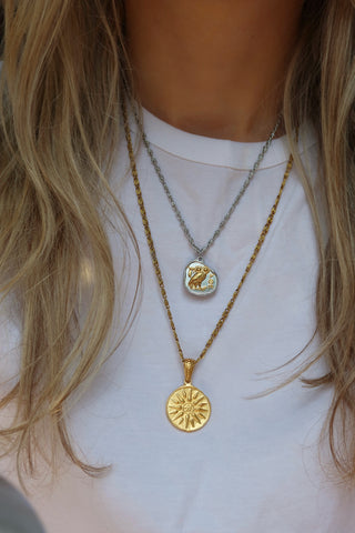 Woman wearing a silver and gold two-tone Athena owl coin pendant necklace and a long gold sun pendant necklace