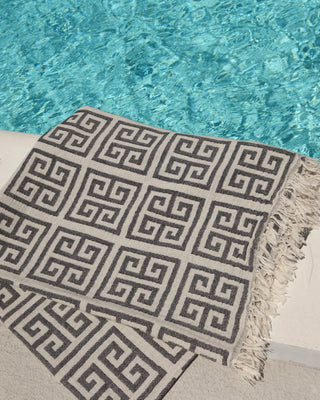 Black and off-white Greek Key meander print cotton towel next to a pool. Greek pestemal towel with fringe