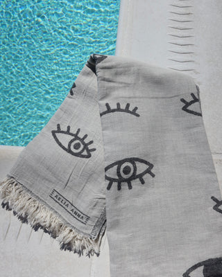 Gray towel with black evil eye pattern by a pool