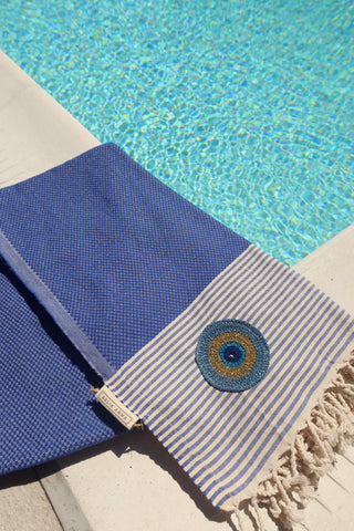 Blue and off-white striped cotton pestemal towel with an embroidered metallic evil eye and fringe trim made in Greece, Greek beach towel