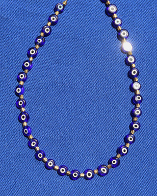 Necklace with blue glass evil eye beads on a blue fabric background