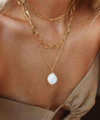 Model wearing a gold necklace stack featuring a baroque pearl pendant necklace on a gold-plated sterling silver chain made in Greece. Greek designer jewelry brand, Greek jewelry, handmade necklace