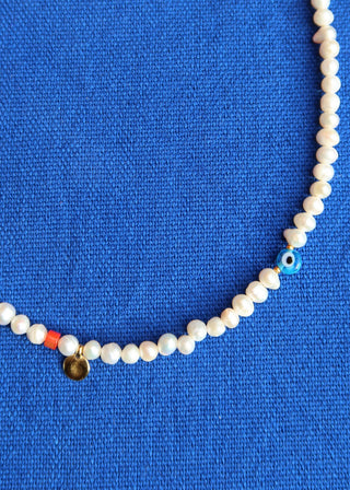 Freshwater pearl necklace with a blue evil eye, red bead, and gold disc charm made in Greece. Greek jewelry at Aegean Essence