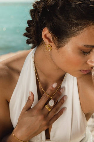 Model wearing a gold necklace stack featuring a baroque pearl pendant necklace on a gold-plated sterling silver chain made in Greece. Greek designer jewelry brand, Greek jewelry, handmade necklace