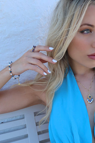 Model wearing a gold-plated drop pendant necklace with an evil eye and freshwater pearls and a greek key motif made in Greece, and a pearl and evil eye greek jewelry bracelet