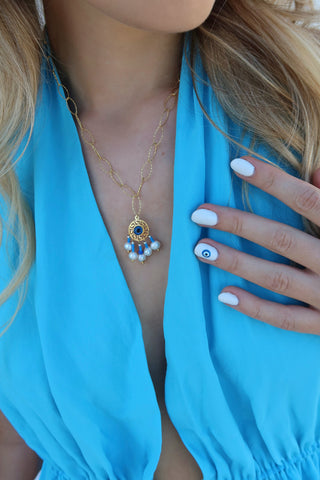 Model wearing a gold-plated drop pendant necklace with an evil eye and freshwater pearls and a greek key motif made in Greece, and a pearl and evil eye greek jewelry bracelet