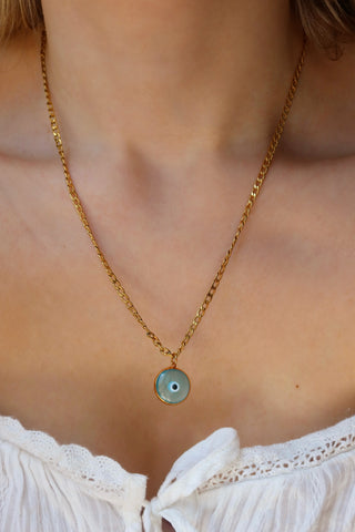 Gold chain necklace with a light blue glass evil eye pendant on a woman. Greek mati jewelry, evil eye necklace made in Greece