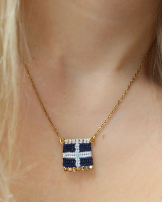 Woman wearing a woven macrame Greek flag necklace with a gold chain and gold bead details made in Greece. Vintage Hellenic Republic flag necklace with turquoise stone and gold embellishments