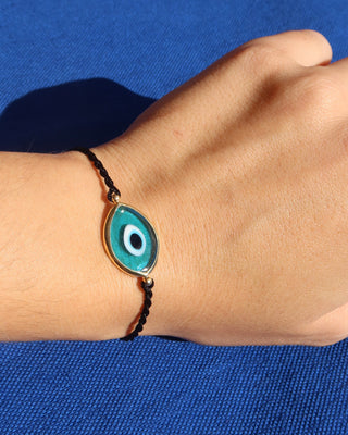 Woman's wrist wearing a turquoise blue Murano glass 18k gold plated evil eye bracelet with an adjustable black woven design made in Greece, Greek evil eye jewelry