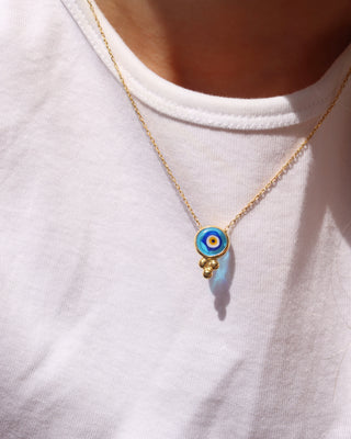 Woman wearing an 18k gold-plated evil eye necklace with a circular transparent blue murano glass evil eye made in Greece, Greek evil eye jewelry