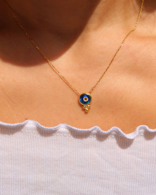 Woman wearing an 18k gold-plated evil eye necklace with a circular transparent blue murano glass evil eye made in Greece, Greek evil eye jewelry