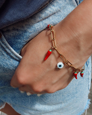 Bracelet with red chili pepper and eye-shaped charms on a wrist against a denim background