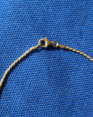 Close-up of a gold chain necklace lobster claw clasp on a textured blue fabric background.