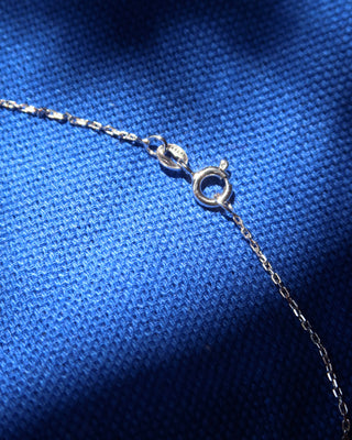Close-up of a silver chain necklace with a spring ring clasp, laid on a textured blue fabric background.