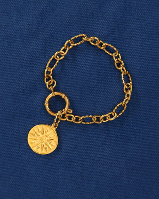 Gold chain bracelet with a Vergina sun coin charm on a blue background made in Greece, Ancient Greek jewelry