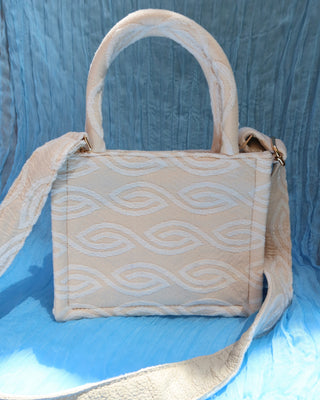 Cream/off-white handbag with two top handles and a crossbody strap with a white eye-shaped wave print woven cotton, made in Greece. Marabu bag worn by Lily Collins and Ashley Park in Emily in Paris Mykonos handbag brand