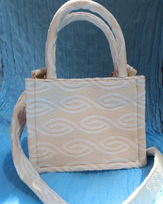 Cream/off-white handbag with two top handles and a crossbody strap with a white eye-shaped wave print woven cotton, made in Greece. Marabu bag worn by Lily Collins and Ashley Park in Emily in Paris Mykonos handbag brand