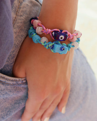 Pink and blue woven rope adjustable bracelets with glass evil eye beads on a wrist, Greek summer jewelry