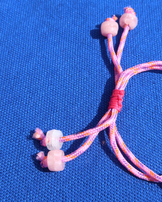Pink braided cord bracelet with beads on a blue fabric background