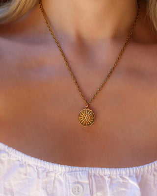 Woman wearing a gold sunburst coin necklace on an infinity chain, ancient Greek coin jewelry