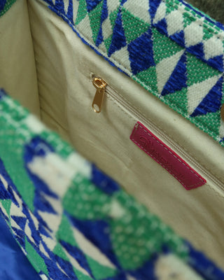 Close-up of a handbag's interior showing a cream-colored fabric lining, a gold zipper pull, a pink brand label, and a green, blue, and white geometric patterned fabric trim.