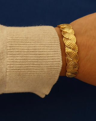 Gold cuff bracelet on a wrist with a braided wave design made in Greece, Greek jewelry
