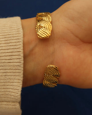 Gold cuff bracelet on a wrist with a braided wave design made in Greece, Greek jewelry