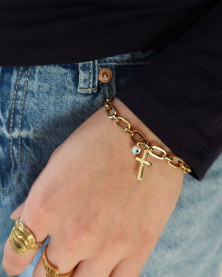 Gold stainless steel chain link bracelet with a cross and white evil eye charm on a woman's wrist. Greek evil eye jewelry made in Greece