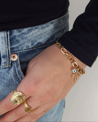 Gold stainless steel chain link bracelet with a cross and white evil eye charm on a woman's wrist. Greek evil eye jewelry made in Greece