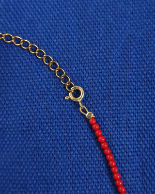 Gold extender with red coral beads on a blue fabric background