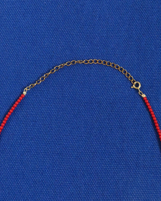 Necklace with red coral beads and gold chain on a blue background