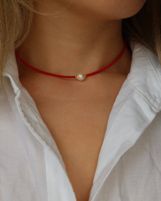 Red beaded coral choker necklace with a pearl pendant worn by a person in a white shirt.