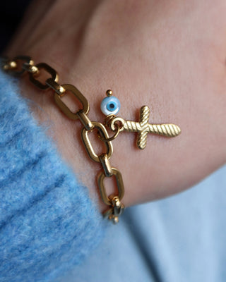 Gold chain link bracelet with a cross charm and white evil eye charm on a wrist. Greek jewelry made in Greece, mati bracelet