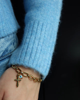Gold chain link bracelet with a cross charm and white evil eye charm on a wrist. Greek jewelry made in Greece, mati bracelet