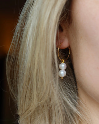 Gold mini hoop earring with pearl drops worn by a person with blonde hair.
