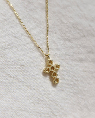 Gold honeycomb pendant cross necklace on a light fabric background
