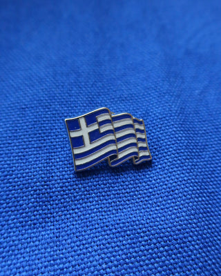 Metal and enamel Greece flag lapel pin on a blue fabric background