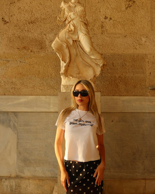 Woman wearing a "hot girls love greek mythology t-shirt" with a black and white polka dot midi skirt standing in front of an ancient greek statue