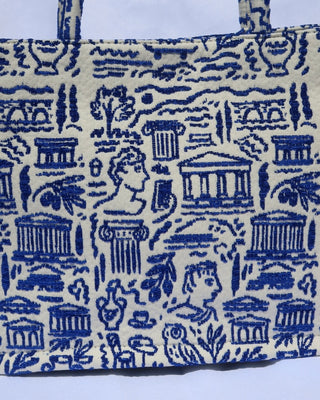 large cream/off-white handbag tote bag with a woven blue Greece print with the Parthenon, ancient Greek sculptures, owls, ionian columns, olive branches, olive trees, and more. Handcrafted bag made in Greece