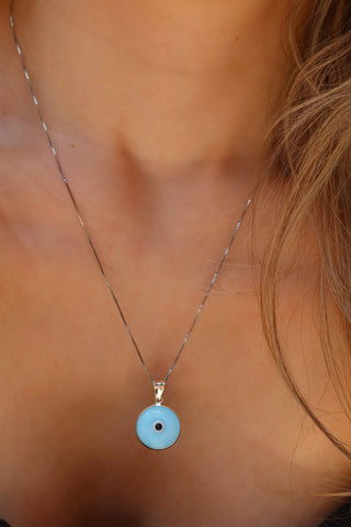 Woman wearing a sterling silver 925 necklace with a light blue glass evil eye round pendant made in Greece. Greek evil eye necklace on a silver chain