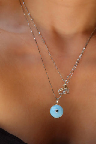 Woman wearing a sterling silver 925 parthenon pendant necklace with a silver chain light blue glass evil eye round pendant made in Greece. Greek evil eye necklace on a silver chain