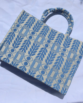 large handbag with woven light blue motif featuring evil eyes, olive branches, and abstract shapes handcrafted in Greece. Greek artisinal handbag