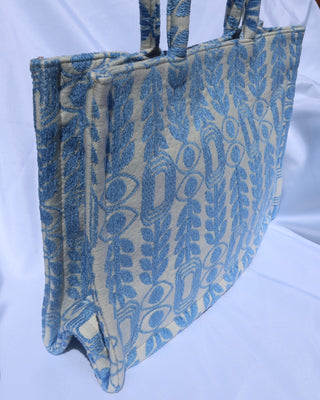 large handbag with woven light blue motif featuring evil eyes, olive branches, and abstract shapes handcrafted in Greece. Greek artisinal handbag