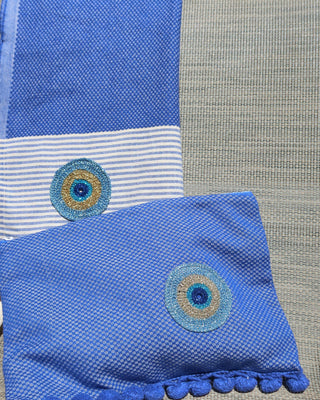 Woven blue clutch bag zipper wet/dry pouch with an embroidered metallic evil eye and a blue pom pom trim and a matching blue and white striped towel with embroidered metallic evil eye appliqué