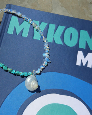 Beaded necklace with howlite and moonstones with a shell pendant on a blue Mykonos Muse book